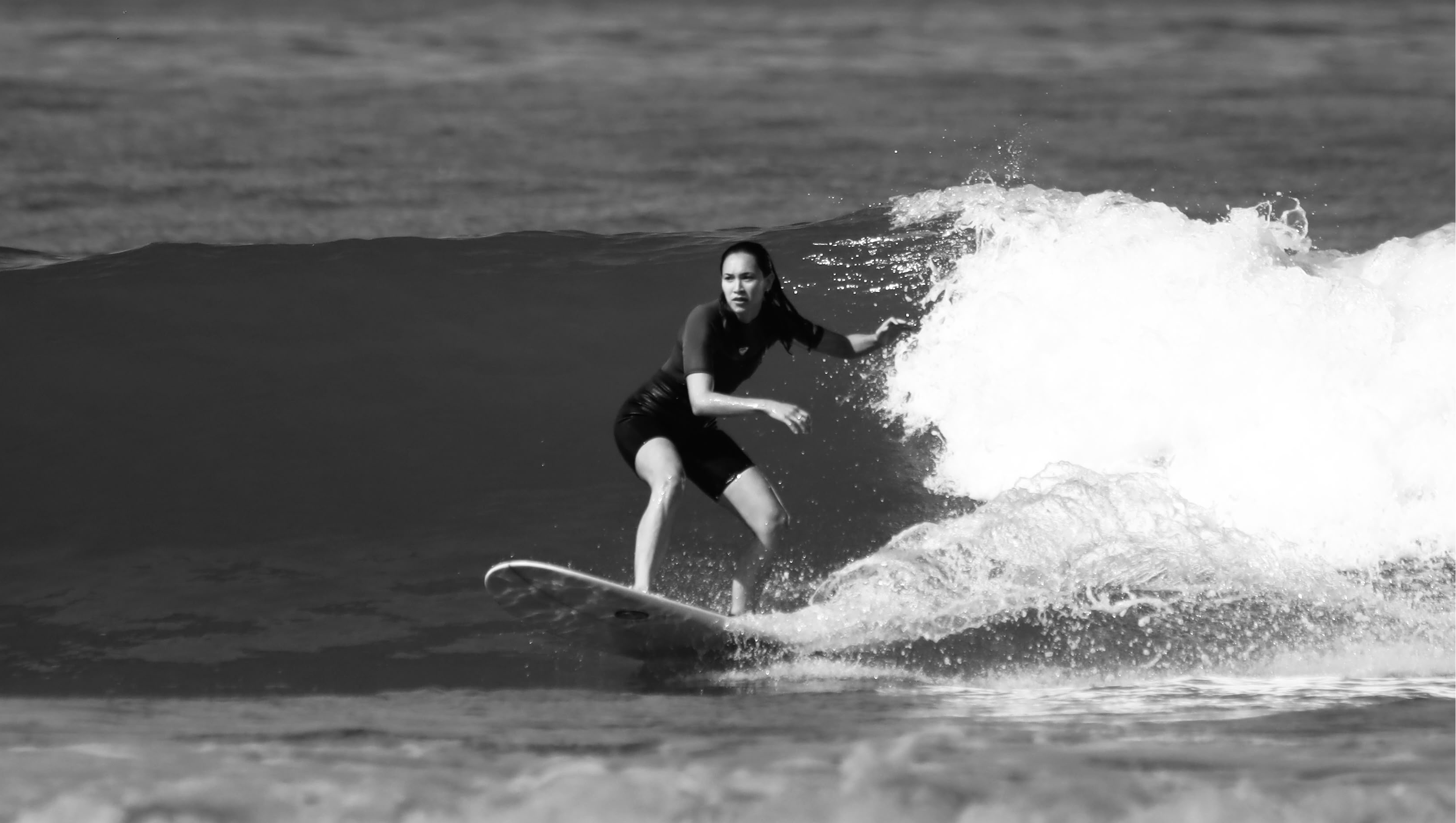 Ingrid praticando surf no mar, em fotografia em preto e branco.